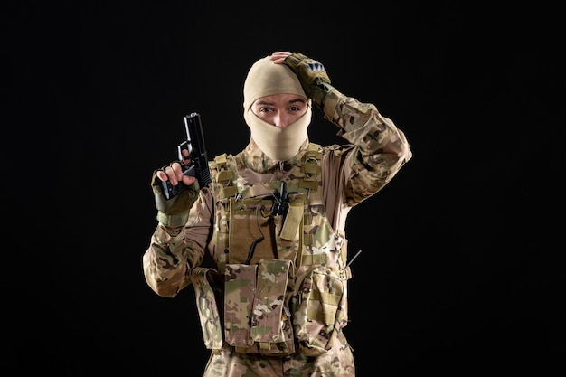 Vooraanzicht jonge soldaat in uniform met pistool op zwarte muur