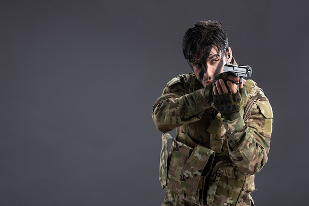 Vooraanzicht jonge soldaat vechten in camouflage met pistool op de donkere muur