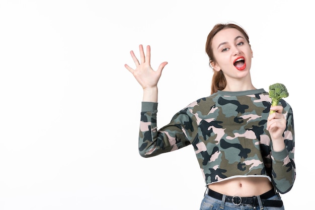 Vooraanzicht jonge vrouw die kleine groene broccoli vasthoudt en op een witte achtergrond rekent lunch maaltijd salade schotel gezondheidszorg voedsel gezondheid gewicht mens