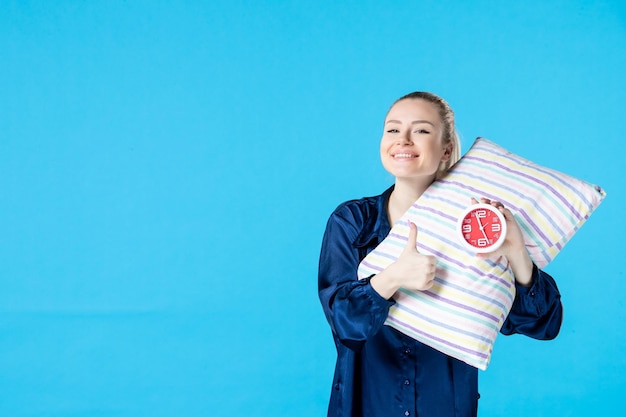 Vooraanzicht jonge vrouw in pyjama met klokken en kussen op blauwe achtergrond moe bed nachtrust slaap droom nachtmerrie laat vrouw