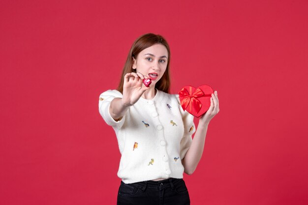 vooraanzicht jonge vrouw met rood hartvormig cadeau op rode achtergrond huwelijk gelijkheid vrouwendag sensueel maart mode vrouwelijk liefde