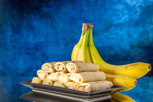 vooraanzicht lekkere gerolde pannenkoeken met bananen op blauwe achtergrond zoet dessert ochtend kleur melk ontbijt cake suiker