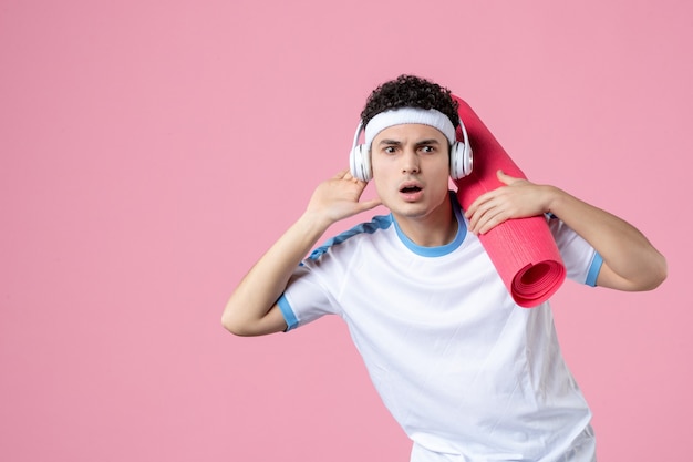 Vooraanzicht luisteren jong mannetje in sportkleren met yogamat