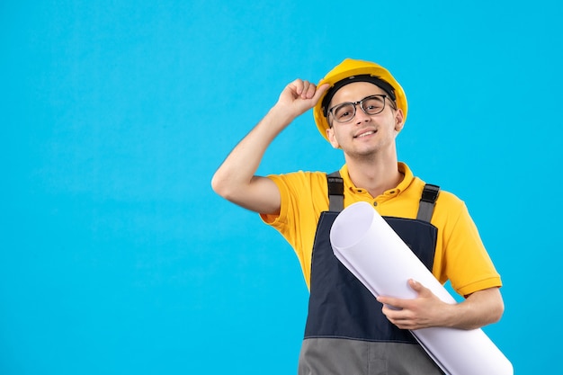 Vooraanzicht mannelijke bouwer in geel uniform met papieren plan op blauw