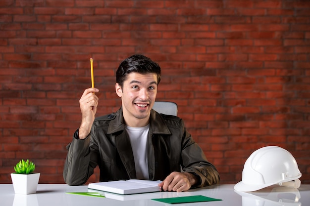 Vooraanzicht mannelijke ingenieur zit achter zijn werkplek aantekeningen schrijven baan bouwer agenda businessplan document succes eigendom zakelijke aannemer