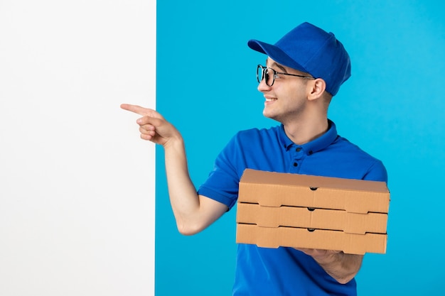 Vooraanzicht mannelijke koerier in blauw uniform met pizzadozen op een blauw