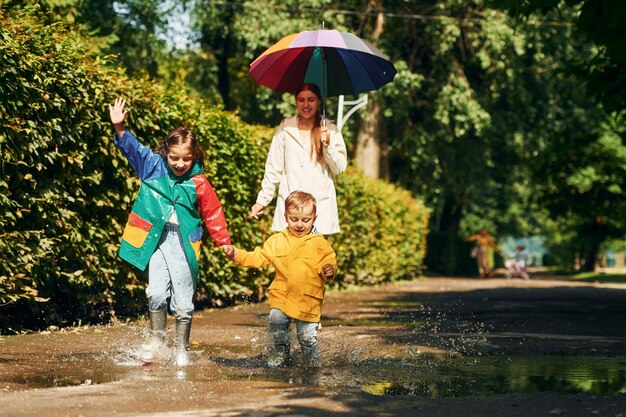 Vooraanzicht Moeder met haar zoontje en dochter wandelen buiten in het park na de regen