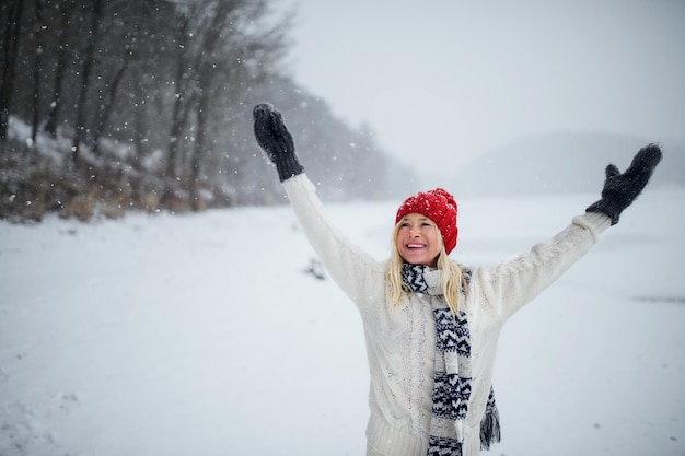 Vooraanzicht portret van gelukkige senior vrouw met muts en wanten buiten staande in de besneeuwde natuur.