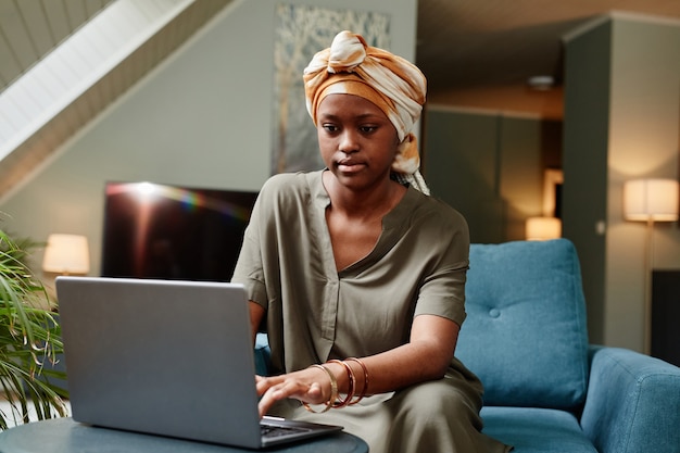 Vooraanzicht portret van jonge Afro-Amerikaanse vrouw die laptop gebruikt terwijl ze thuis kopieerruimte op kantoor werkt