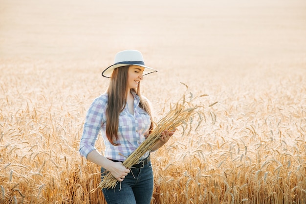 Vooraanzicht portret van jonge vrouw boer met hoed over gouden tarweveld met hoop tarwe en...