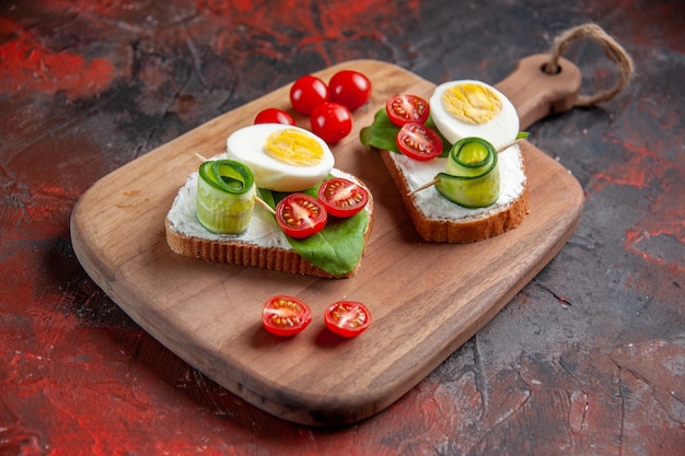 vooraanzicht smakelijke eiersandwiches met rode tomaten op snijplank donkerrode achtergrond lunch toast snack sandwich voedsel brood maaltijd burger