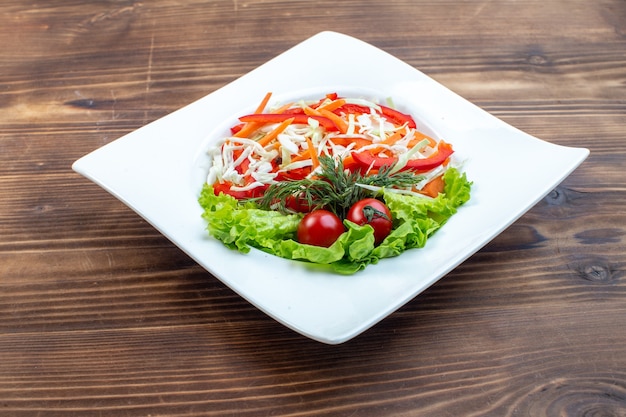 Vooraanzicht smakelijke groentesalade met groene salade en kool binnen plaat op bruine oppervlakte
