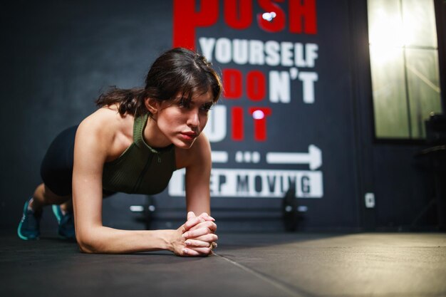 Vooraanzicht van aantrekkelijke jonge vrouw poseert in plankpositie in sportschool Motivatieconcept voor gezondheidszorg