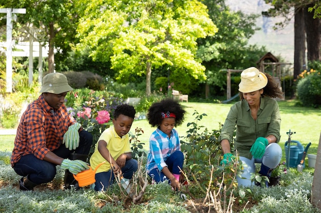 Vooraanzicht van Afro-Amerikaans echtpaar met hun jonge zoon en dochter in de tuin, samen tuinieren en planten water geven. Familie genieten van tijd thuis, lifestyle concept