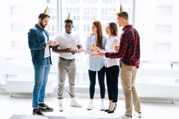 Vooraanzicht van business team van gelukkige multi-etnische ondernemers met Bengaalse lichten en glazen champagne op corporate party op achtergrond van raam en stadsgezicht met wolkenkrabbers