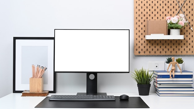 Vooraanzicht van computer met leeg scherm en kantoorbenodigdheden op witte tafel in modern kantoor aan huis.