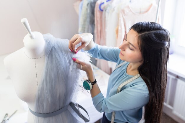 Vooraanzicht van de succesvolle eigenaar van de naaister van het huwelijk meten materialen op mannequin in kantoor of workshop.