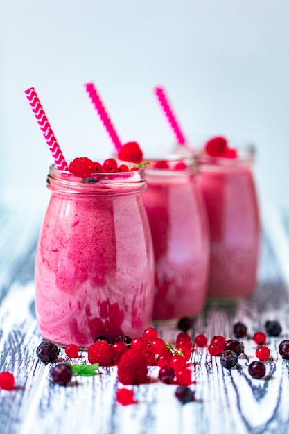 Vooraanzicht van drie bessen milkshakes in glazen potten met ingrediënten op houten tafel