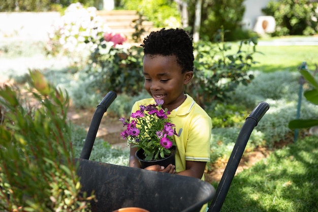 Vooraanzicht van een Afro-Amerikaanse jongen in de tuin, naast een kruiwagen met een plant. Familie genieten van tijd thuis, lifestyle concept