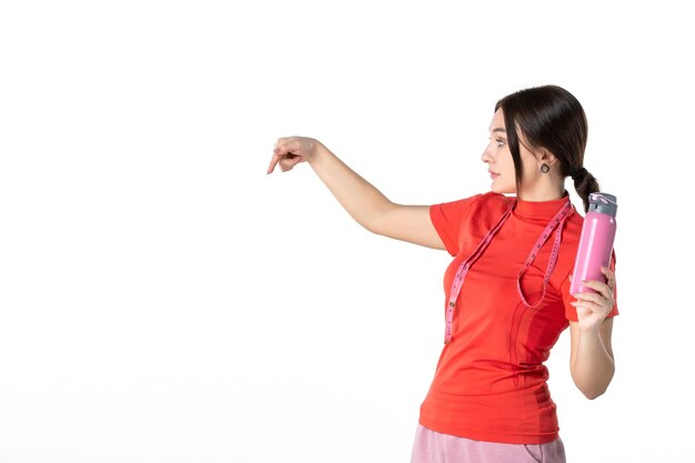 Vooraanzicht van een druk jong meisje in een blouse die een meter vasthoudt en een thermoskan toont die iets op een witte achtergrond wijst