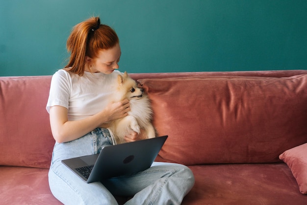 Vooraanzicht van een gelukkige jonge vrouw die werkt op een laptopcomputer die op een comfortabele bank zit te knuffelen schattig