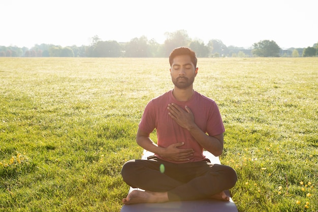 Vooraanzicht van een jonge man die buiten mediteert op yogamat