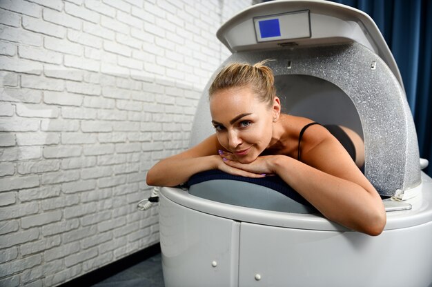 Vooraanzicht van een jonge vrouw die ontspant terwijl ze een wellness-spa-capsulebehandeling krijgt in een moderne spa-kliniek. detailopname