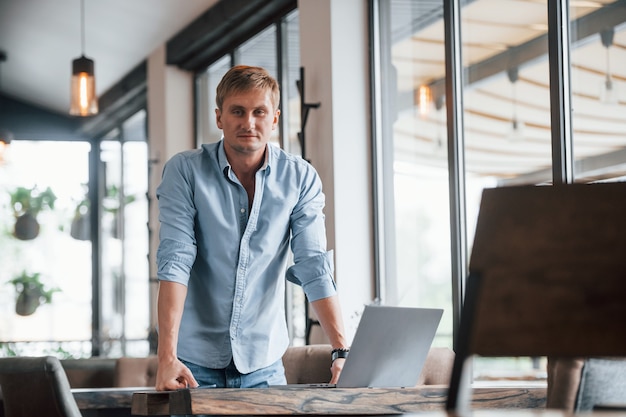 Vooraanzicht van een man die overdag in een modern café zit met zijn laptop.