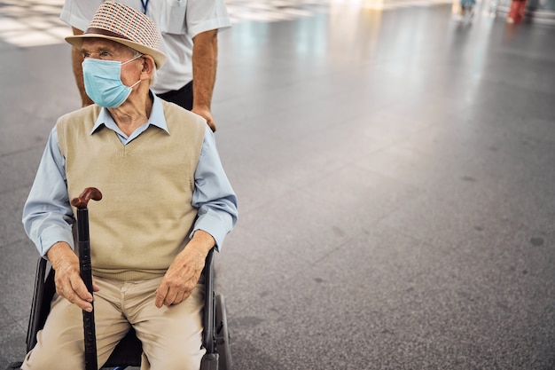 Vooraanzicht van een man met een wandelstok in zijn hand die in een rolstoel zit