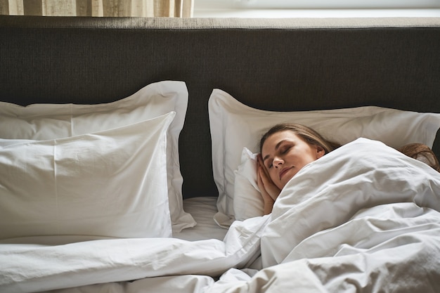 Vooraanzicht van een mooi rustig blond Kaukasisch meisje dat op haar zij in bed ligt