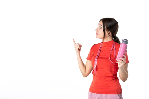 Vooraanzicht van een nieuwsgierig jong meisje in een opnieuw oranje blouse die meter vasthoudt en een thermoskan toont die iets op een witte achtergrond richt