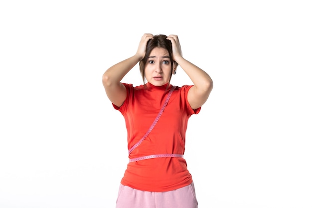 Vooraanzicht van een verraste jonge dame in het opnieuw kleuren van een blouse en met meter op haar taille op een witte achtergrond