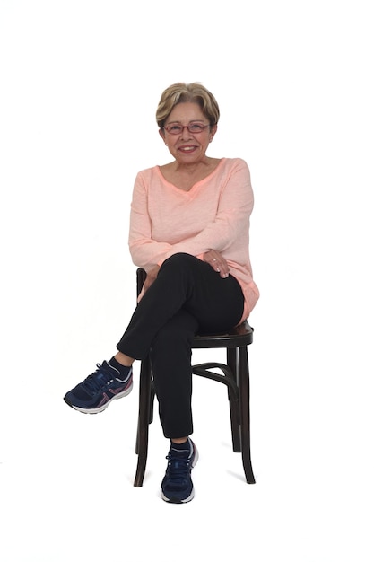 Vooraanzicht van een volledig portret van een gelukkige senior vrouw zittend op een stoel gekleed in sportkleding benen gekruist op een witte achtergrond