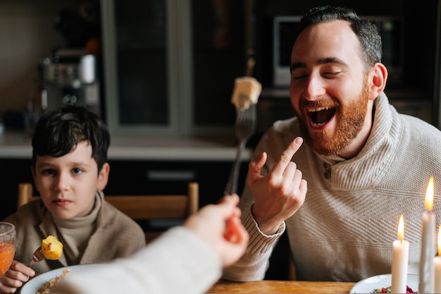 Vooraanzicht van een vrolijk jong gezin dat voor de gek houdt aan een feestelijke kersttafel tijdens een familiefeestje