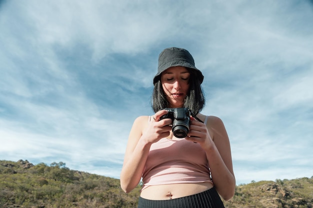 Vooraanzicht van een vrouw die in de natuur staat en haar camera controleert met de lucht achter haar en kopieer ruimte
