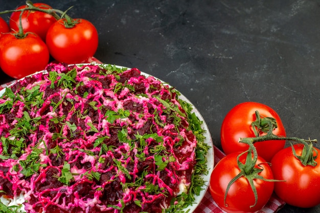 Vooraanzicht van heerlijke salade op rode gestripte handdoek en verse tomaten met stengels op zwarte achtergrond