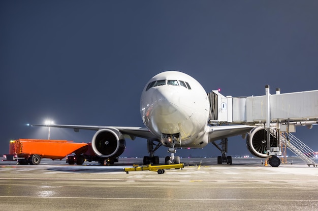 Vooraanzicht van het witte widebody passagiersvliegtuig bij de luchtbrug op het nachtluchthavenschort