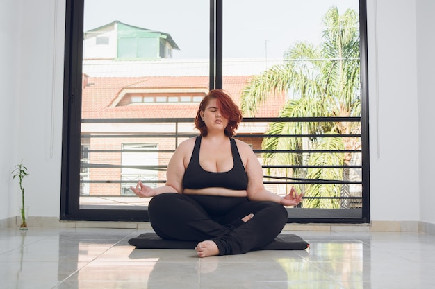 Vooraanzicht van jonge latin plus size vrouw zitten lotus pose asana binnenshuis doen