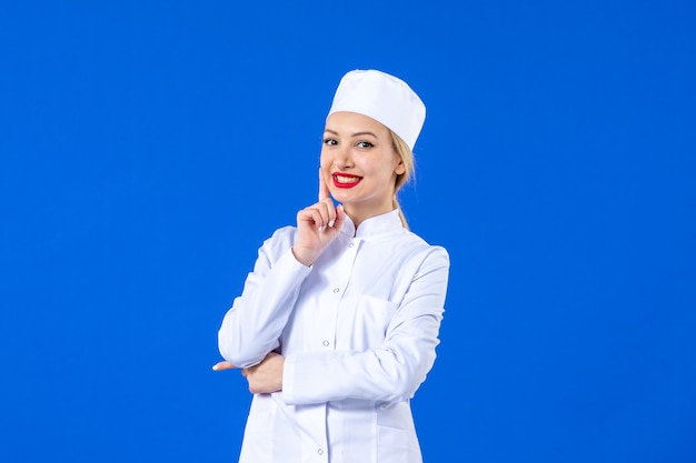 vooraanzicht van jonge verpleegster in wit medisch pak op blauwe muur