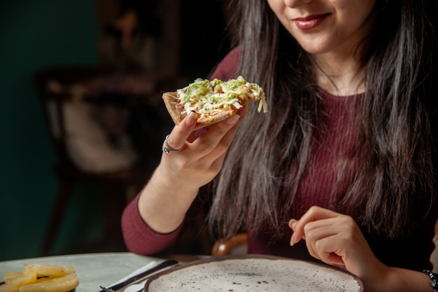 Vooraanzicht van lachende jonge vrouw die een plakje heerlijke pizza eet, consumeert fastfood