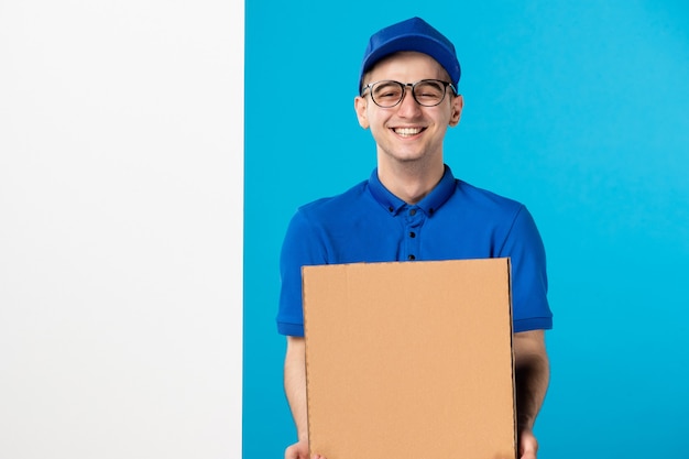 Vooraanzicht van lachende mannelijke koerier in blauw uniform met pizza op blauwe muur