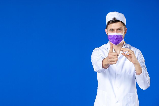 Vooraanzicht van mannelijke arts in medisch kostuum en masker met vaccin en injectie op blauw
