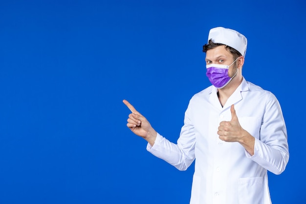 Vooraanzicht van mannelijke arts in medisch kostuum en paars masker op blauw