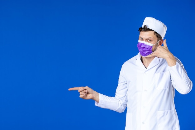 Vooraanzicht van mannelijke arts in medisch kostuum en paars masker op blauw