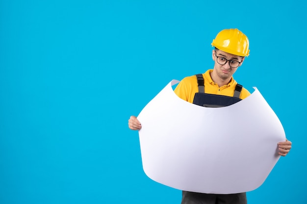 Vooraanzicht van mannelijke bouwer in geel uniform met plan op blauw