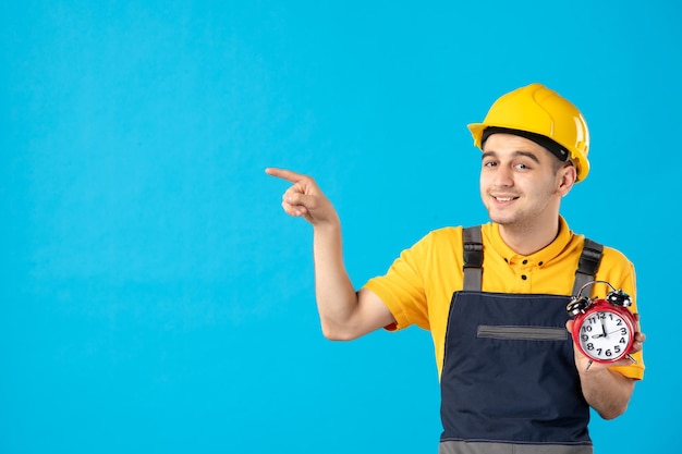 Vooraanzicht van mannelijke werknemer in geel uniform met klokken op blauw