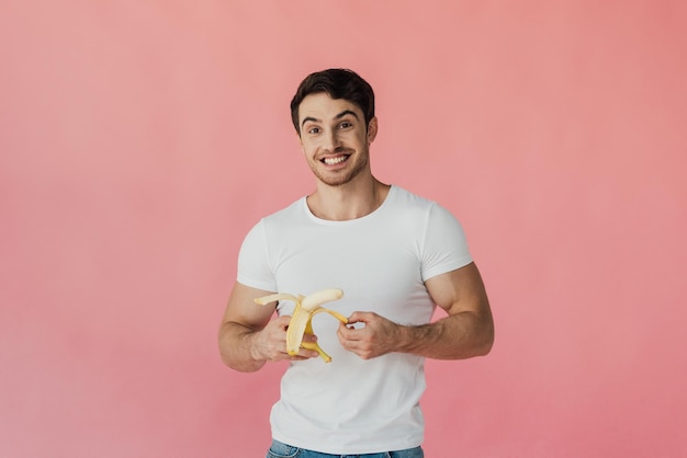 Vooraanzicht van opgewonden gespierde man in wit t-shirt met banaan geïsoleerd op roze