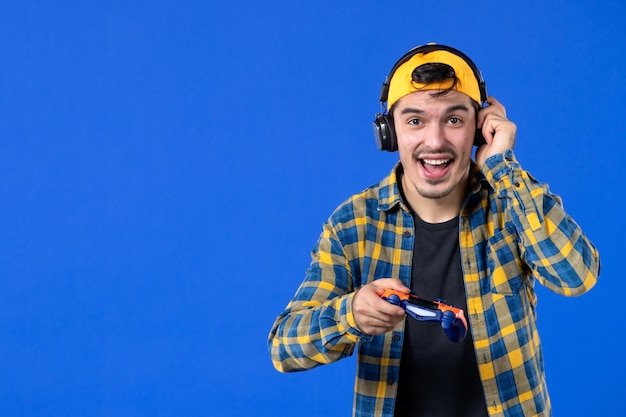 Vooraanzicht van opgewonden mannelijke gamer met oranje gamepad die videogame speelt op blauwe muur