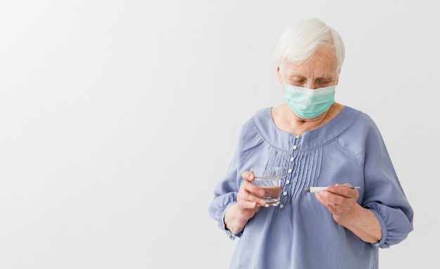 Foto vooraanzicht van oudere vrouw met de medische thermometer van de maskerholding met exemplaarruimte