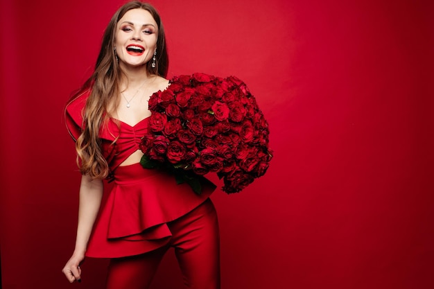 Vooraanzicht van prachtige vrouw in rode jurk met make-up houden mooi boeket rozen camera kijken en glimlachen mooi model poseren op rode geïsoleerde achtergrond Concept van Valentijnsdag